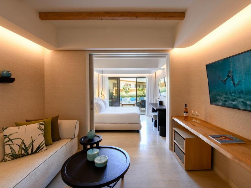 Camera d'hotel moderna con divano, tavolo e vista sulla camera da letto con terrazza.