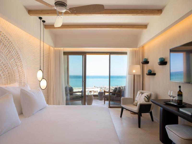 Camera d'hotel moderna con letto grande e vista mare tramite porta scorrevole in vetro.