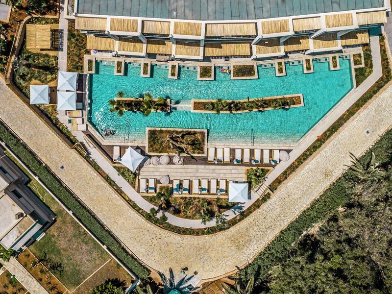 Vista aerea di una grande piscina triangolare con lettini e vegetazione intorno.