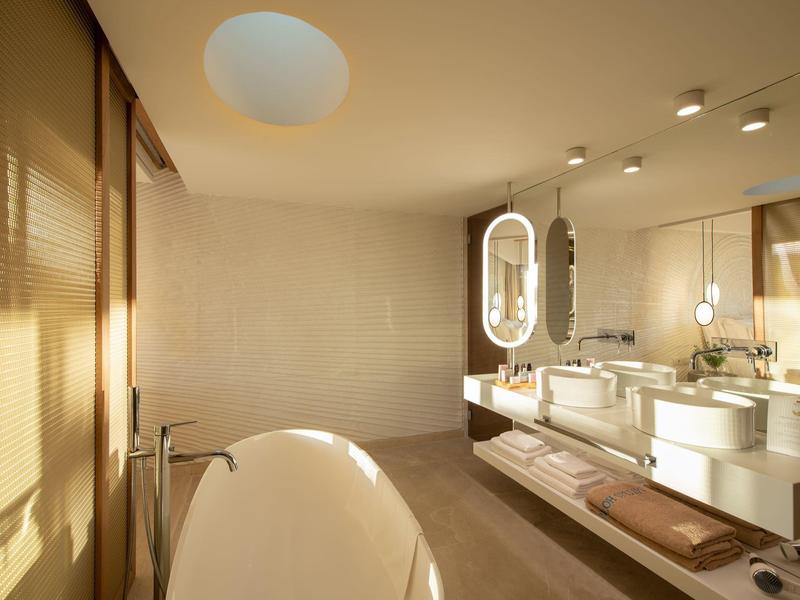 Bagno moderno con vasca da bagno freestanding e doppi lavandini illuminati da luce calda.