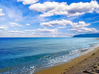 Strand mit sanften Wellen, blauem Himmel und weißen Wolken, ideal für einen Urlaub am Meer.