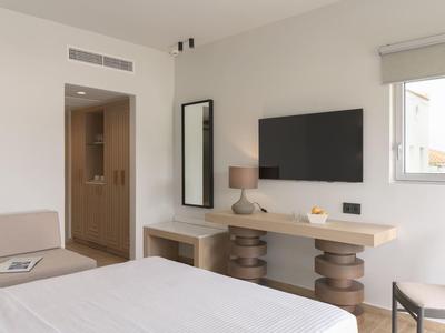 Helles Hotelzimmer mit Fernseher, Schreibtisch, Lampe und Fenster mit Außenblick.