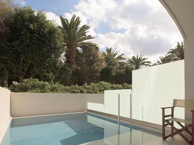 Moderner Hotelpool mit Glasgeländer, weißen Wänden und Stuhl unter blauem Himmel.
