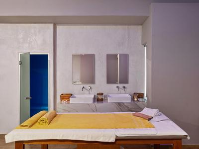 Modernes Hotelzimmer mit einem Behandlungsbett, gelber Decke und einem Bad mit zwei Waschbecken.