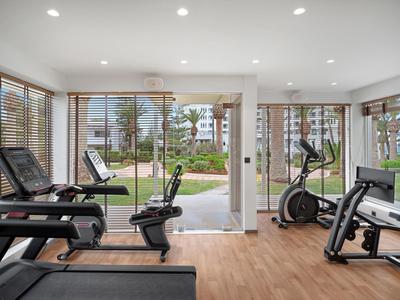 Moderner Fitnessraum mit Laufbändern, Fahrrädern und großen Fenstern mit Blick auf Garten.