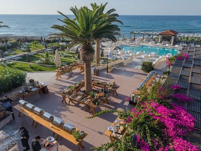 Moderner Hotelpool mit Liegestühlen, Palmen und Blick auf das blaue Meer bei klarem Himmel.