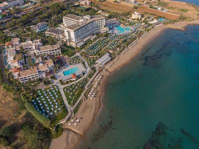 Luftaufnahme eines Strandresorts mit mehreren Gebäuden, Pool und Blick auf das Meer.