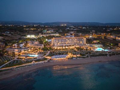 Beleuchtetes Hotel an der Küste mit Pool und Strand in der Abenddämmerung.