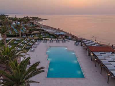 Ein ruhiger Poolbereich eines Hotels am Meer bei Sonnenuntergang mit Liegen und Palmen.