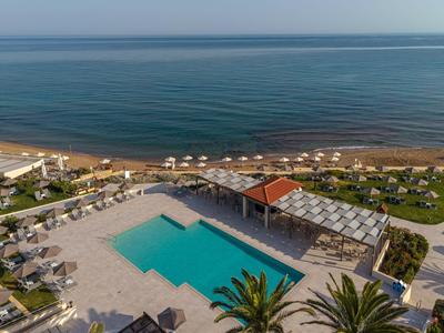 Hotelpool mit Liegestühlen und Blick auf das ruhige Meer und den Sandstrand.
