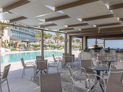 Überdachte Terrasse mit Stühlen und Tischen neben einem Pool in einem Hotel.