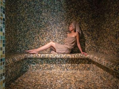 Frau entspannt auf einer Bank in einem mit Mosaikfliesen ausgekleideten Spa-Raum.