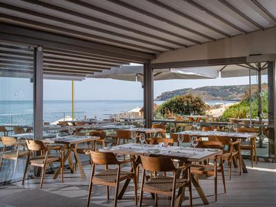 Offene Terrasse eines Restaurants mit Holztischen und Blick auf Meer und Küste.