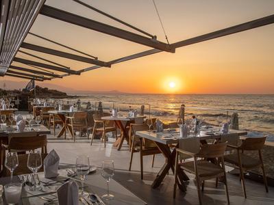 Terrasse eines Hotels mit gedeckten Tischen am Strand bei Sonnenuntergang.