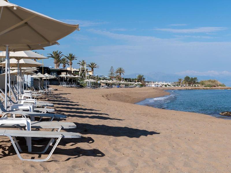 Písčitá pláž s lehátky pod slunečníky u bleděmodrého moře.