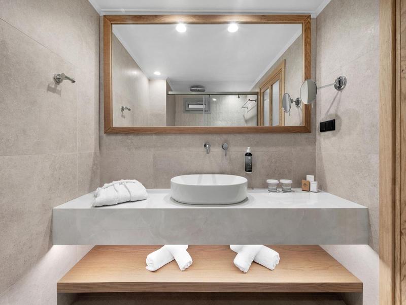 Moderní koupelna s kulatým umyvadlem a velkým zrcadlem v dřevěném rámu.