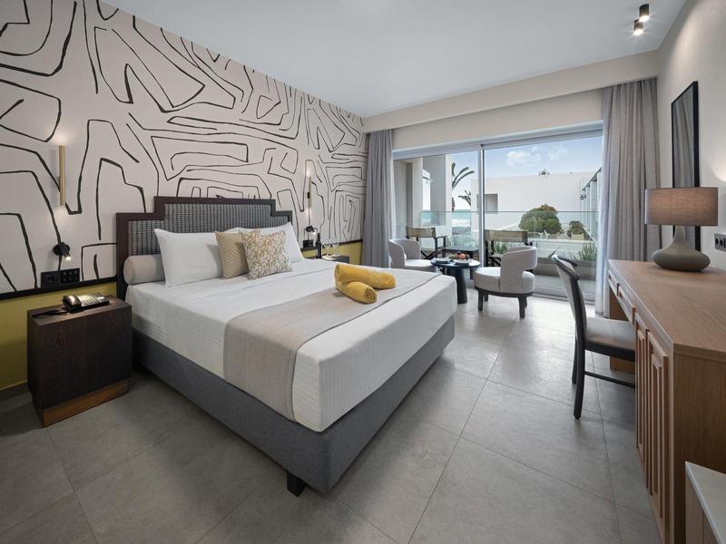 Moderní hotelový pokoj s velkou postelí, jednoduchým zařízením a výhledem na venkovní terasu.