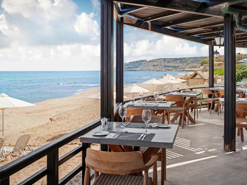 Terasa restaurace s výhledem na písečnou pláž a bílé slunečníky.