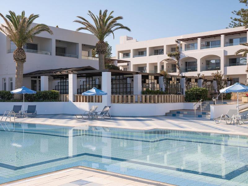 Čistý venkovní bazén s lehátky a bílá budova s palmami pod modrou oblohou.