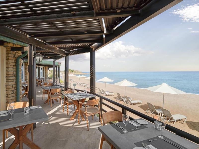 Restauranční terasa s stolem, židlemi a slunečníky na pláži s výhledem na moře.