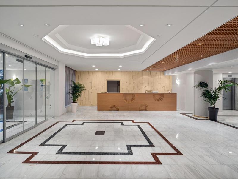 Elegantní hotelová recepce s mramorovou podlahou, dřevěnou recepcí, zelenými rostlinami a sklem.