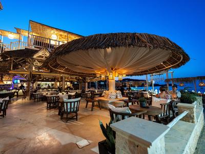 Otevřená restaurace u moře s velkými slunečníky a stoly za soumraku.