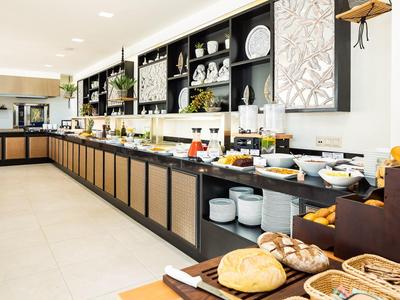 Heller Frühstücksraum mit langem Buffet, frischem Gebäck, Obst und Getränken in modernen Regalen.