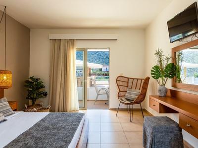 Helles Schlafzimmer mit Bett, Sessel, TV, Pflanzen und Balkon mit Bergblick.