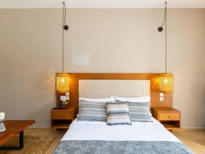 Modernes, helles Schlafzimmer mit Holzbett, grauen Kissen, Bettdecke und zwei hängenden Lampen.