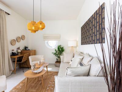 Helles Wohnzimmer mit weißen Möbeln, Holzkommode, Teppich und gelben Hängeleuchten.