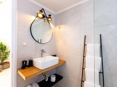 Modern bathroom with sink on wooden shelf, round mirror, and towel ladder.