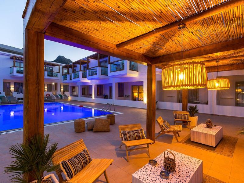Cozy outdoor lounge with wooden furniture and illuminated pool in a hotel complex at dusk.