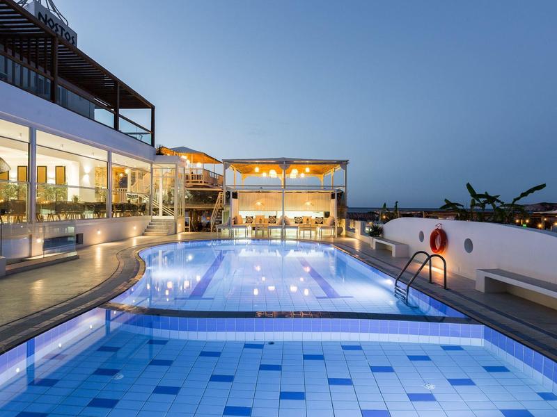 Modern pool area with loungers and beds in front of hotel rooms under clear sky.