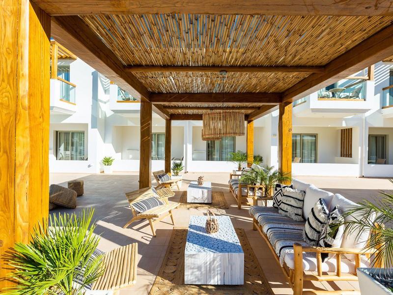 Modern outdoor area with wooden pergola, seating, and white buildings in the background.