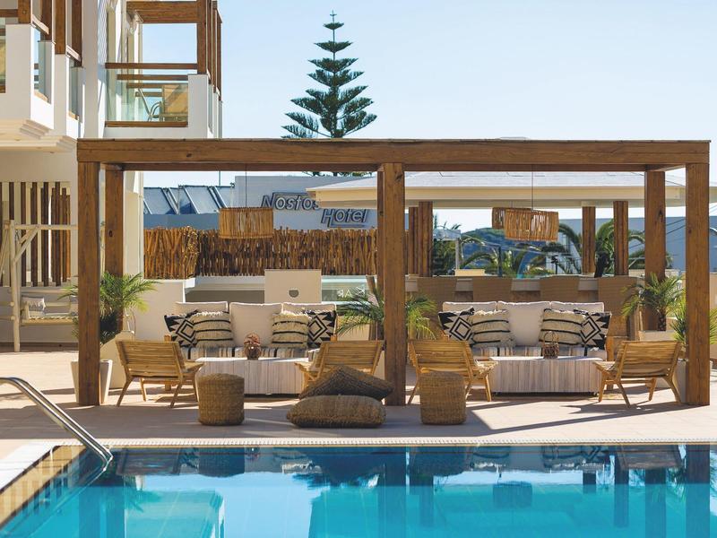 Modern outdoor area with pool, wooden pergola, and comfortable seating in a hotel garden.