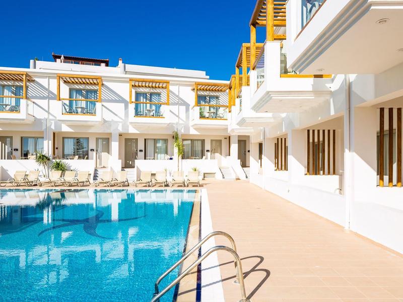 Bright hotel with pool and lounge chairs under clear blue sky.