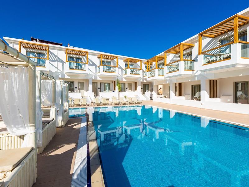 Modern hotel pool area with blue water and white sun loungers under a clear blue sky.