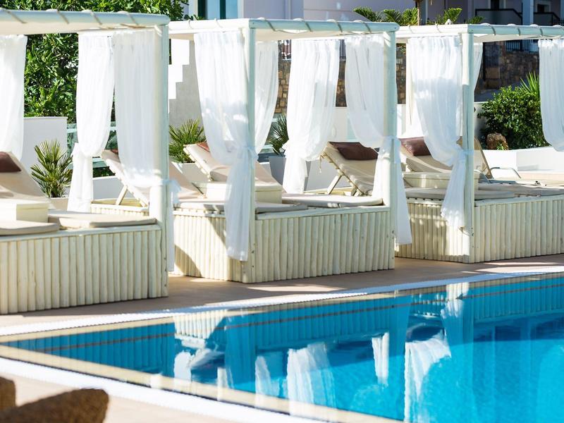 White lounge beds with curtains beside a blue hotel pool in sunny weather