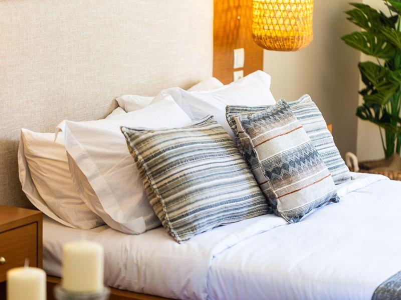Cozy white bed with multiple striped pillows and yellow hanging lamp in bedroom.