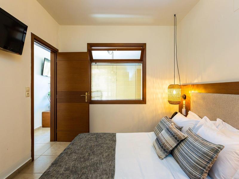 Bedroom with double bed, wall-mounted TV, and open wooden door in the background.