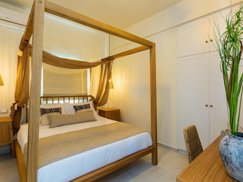 Bright bedroom with canopy bed, wooden furniture, and a vase with green plants.