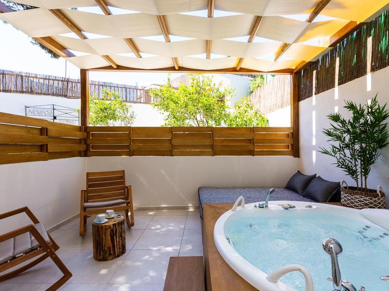 Cozy terrace with hot tub, sofa, and wooden chairs, surrounded by wooden walls and plants.