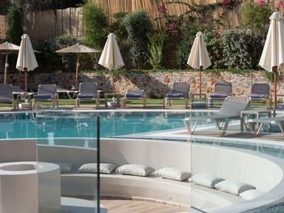 Panchina rotonda con cuscini davanti a una piscina con lettini e ombrelloni.