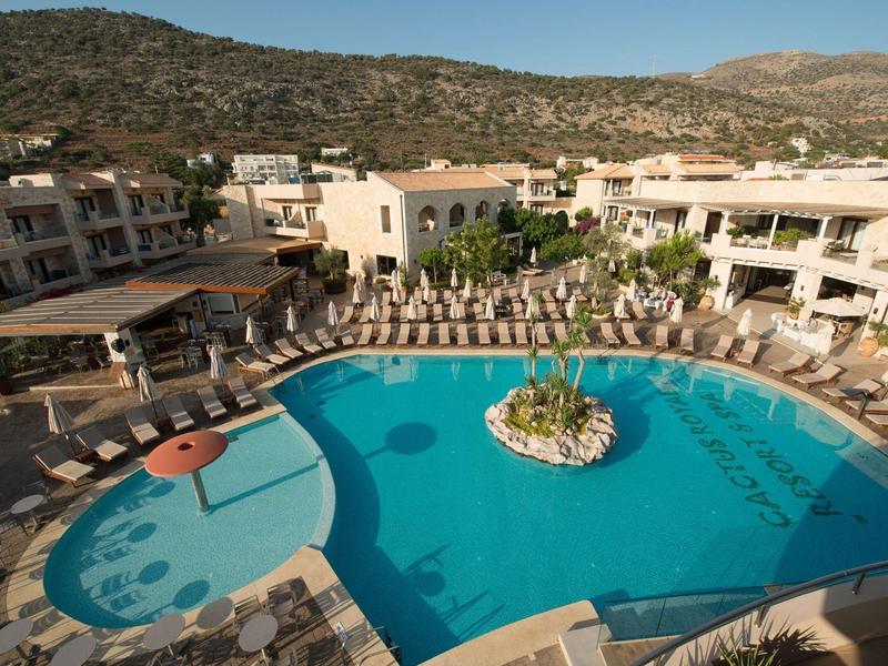 Gran piscina del hotel con tumbonas, rodeada de edificios y colinas al fondo.