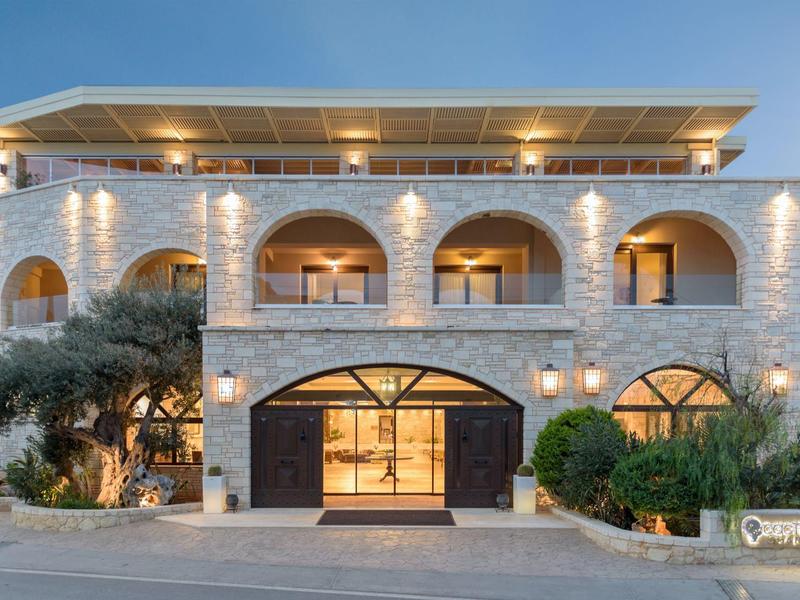 Hotel elegante de varios pisos con fachada de piedra, grandes arcos y luces exteriores cálidas al anochecer.