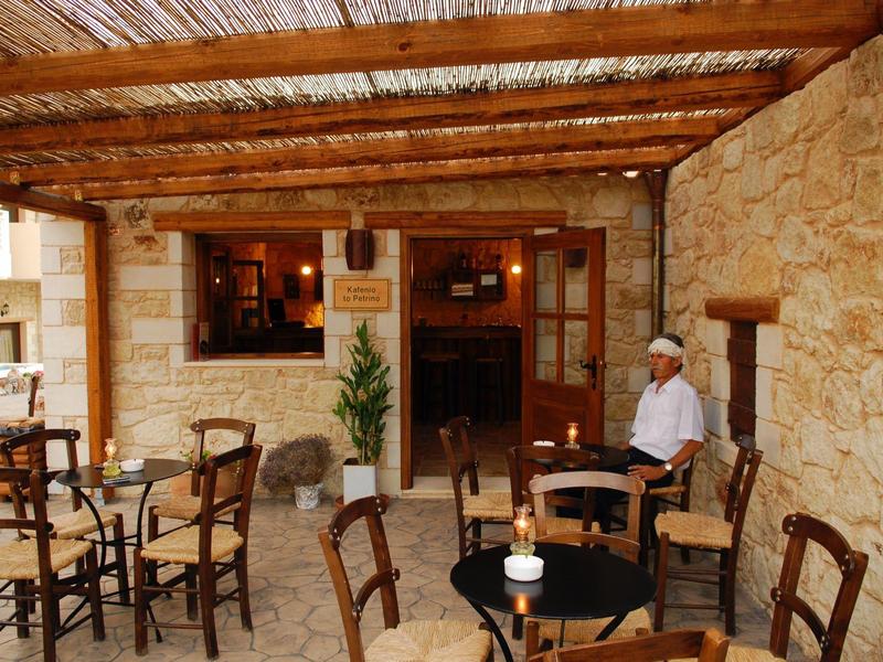 Terraza acogedora con mesas y sillas de madera junto a una fachada de piedra, un hombre sentado relajado.