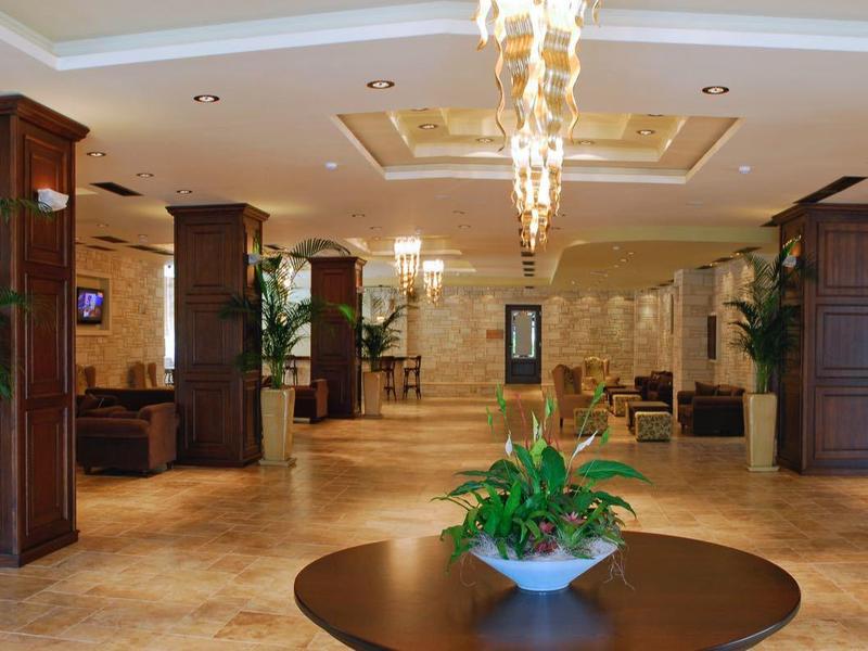 Amplio vestíbulo de hotel con suelo de mármol, columnas, áreas de descanso y arreglo floral central.