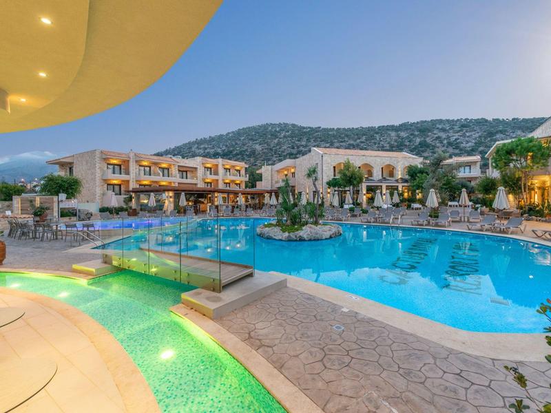 Gran piscina del hotel con agua iluminada y edificios de varios pisos alrededor al atardecer.