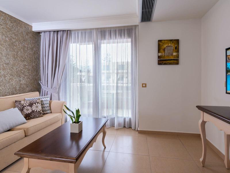 Habitación de hotel luminosa con sofá cómodo, cortinas y televisor de pantalla plana en la pared.