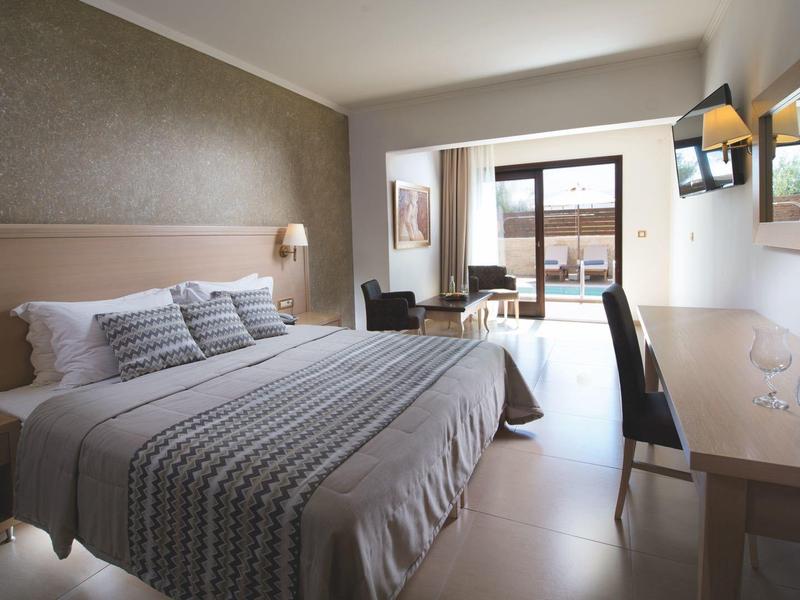 Habitación de hotel luminosa con cama grande, escritorio, silla y terraza con vista al mar.